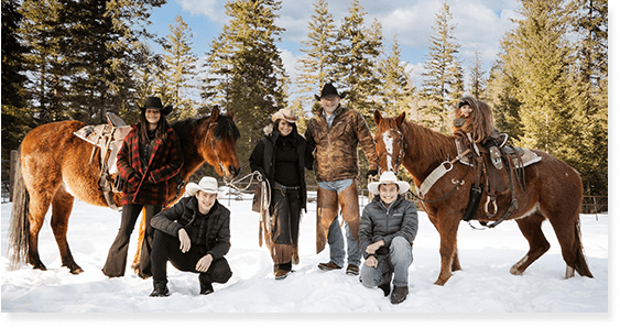 A group of people standing next to horses in the snow.